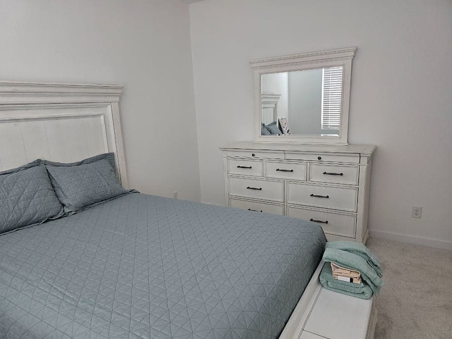 Furnished bedroom with queen bed, dresser, and mirror